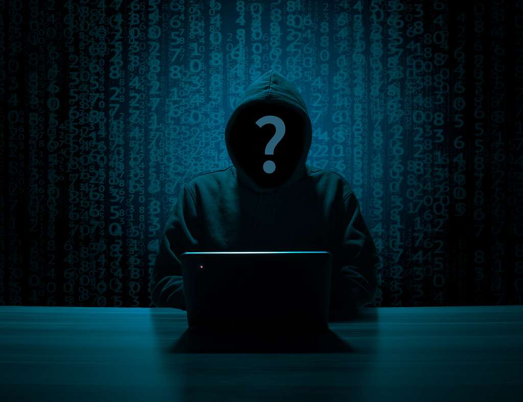 Mysterious man in a hoodie behind a computer. Image of a hacker.